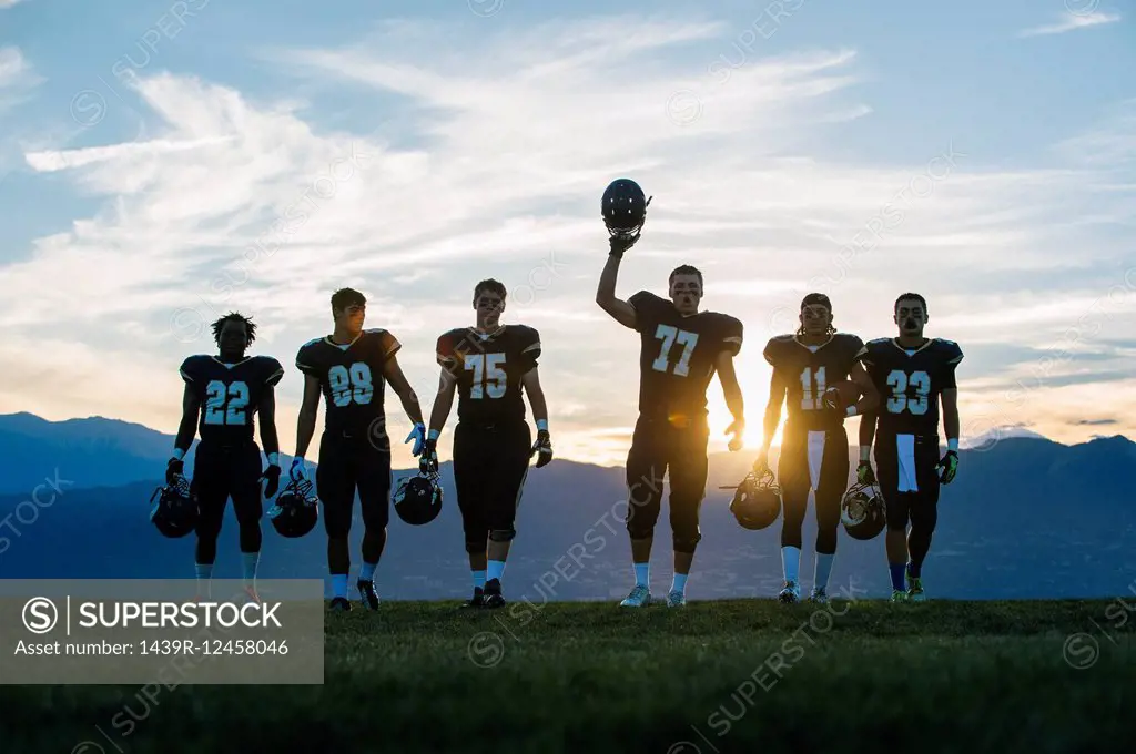 Silhouetted teenage and young male american football team celebrating at dusk