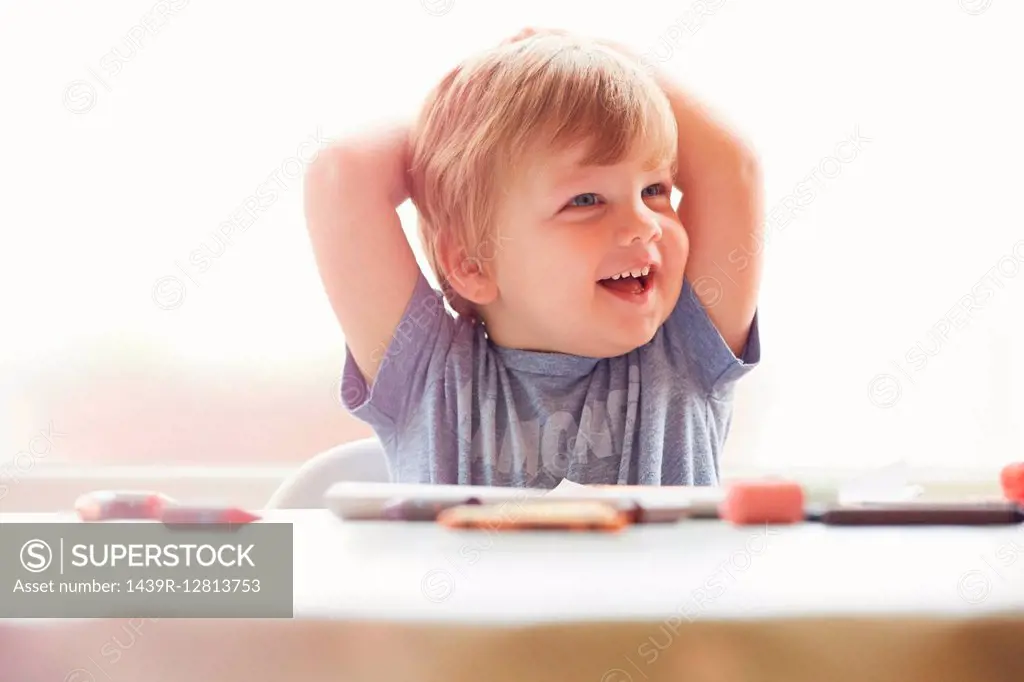 Boy sitting at table hands behind head, looking away smiling
