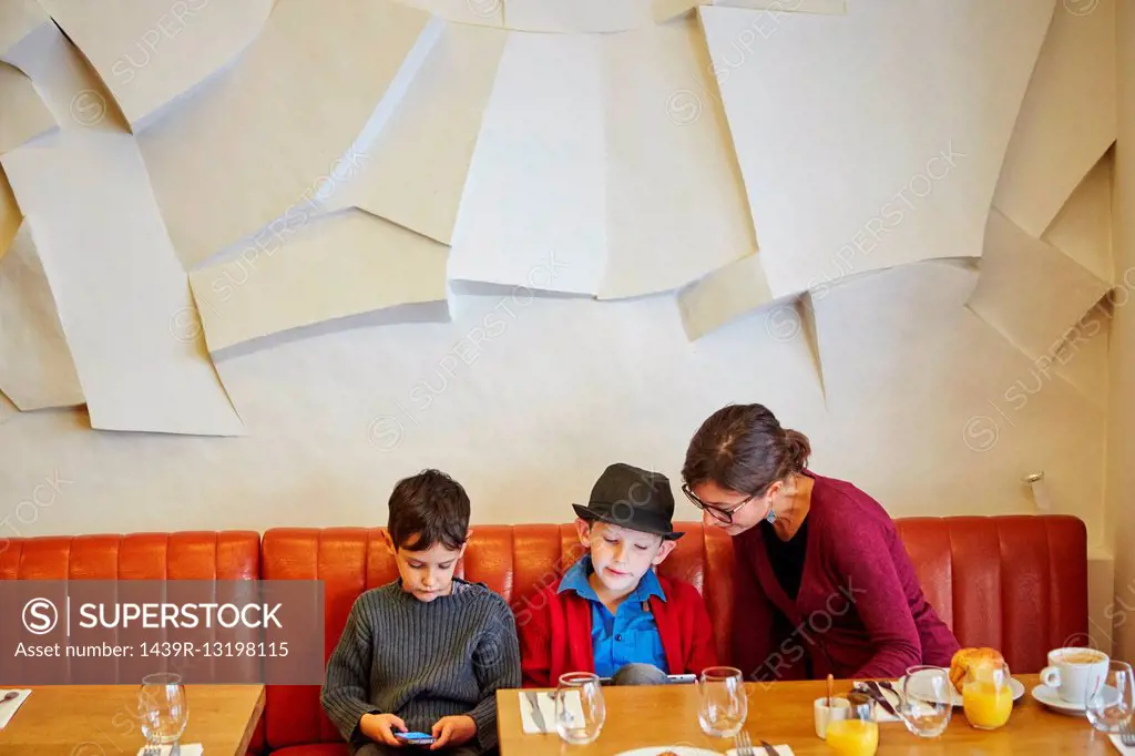 Mother and sons using digital tablet and smartphone in restaurant