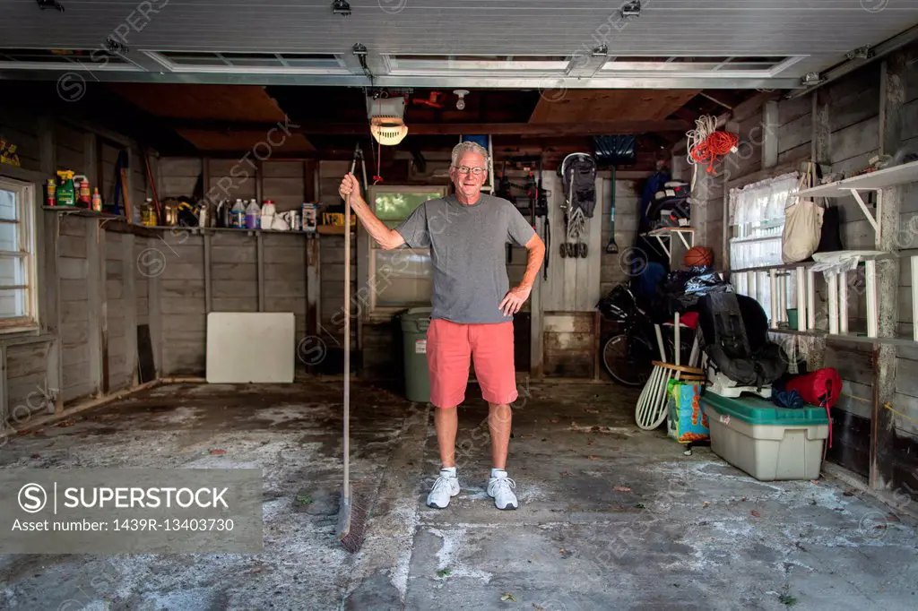 Portrait of senior man standing in garage holding broom