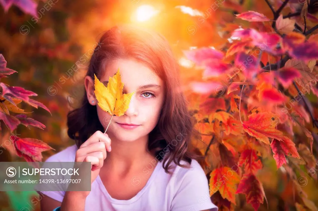 Portrait of young girl in rural setting, holding leaf in front of eye