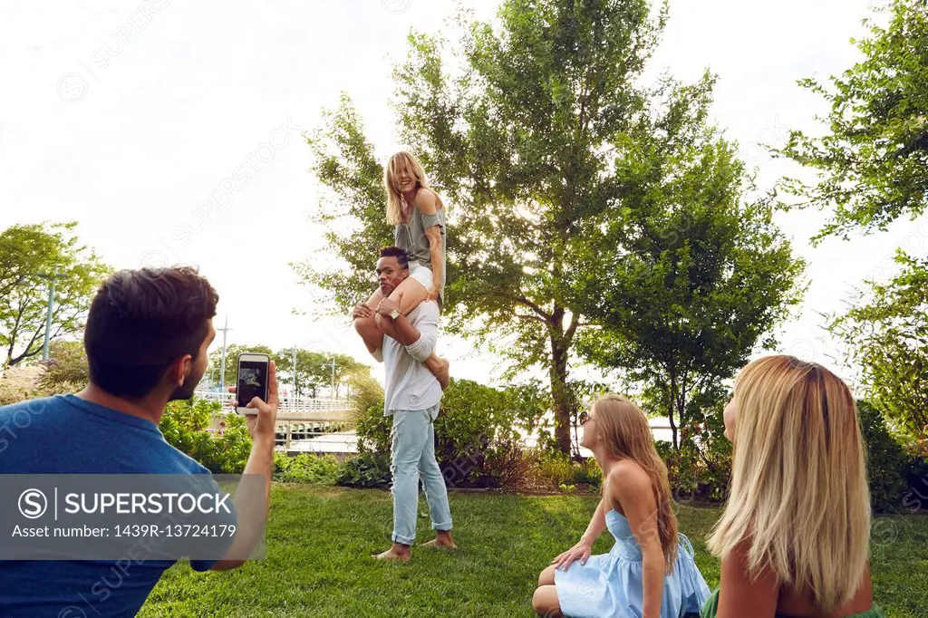 Young man photographing shoulder carrying friends in park