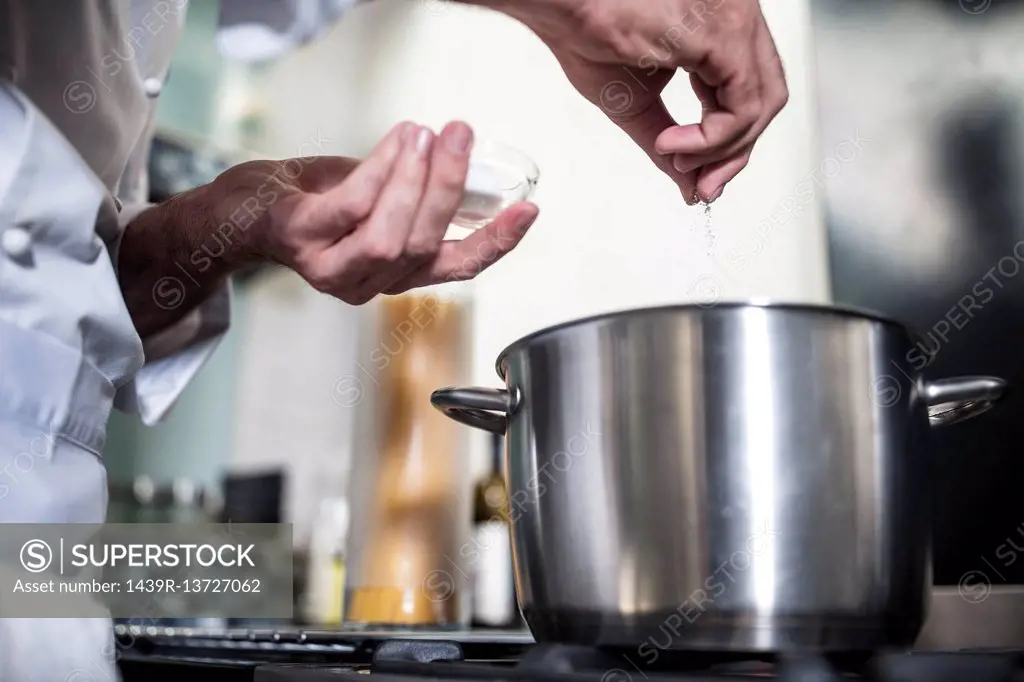 Chef putting salt in pan of water on stove, close-up