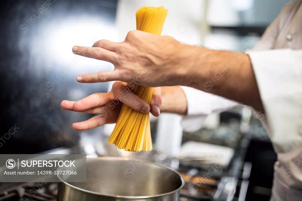 Chef putting spaghetti in saucepan on stove, close-up, overhead view