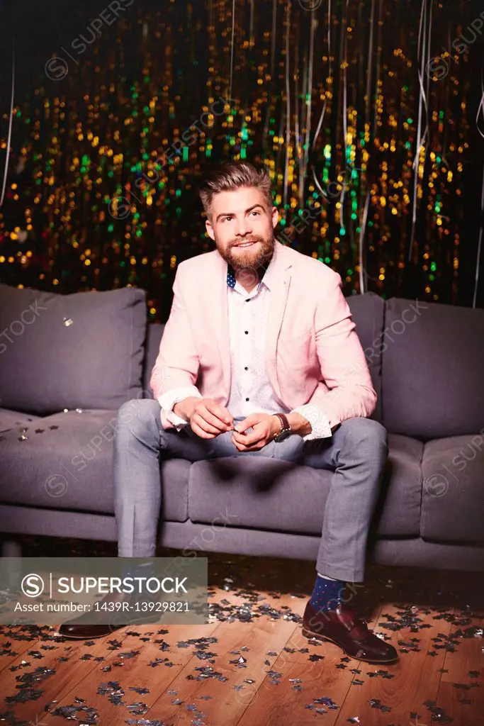 Man sitting on sofa at party, glitter covering floor
