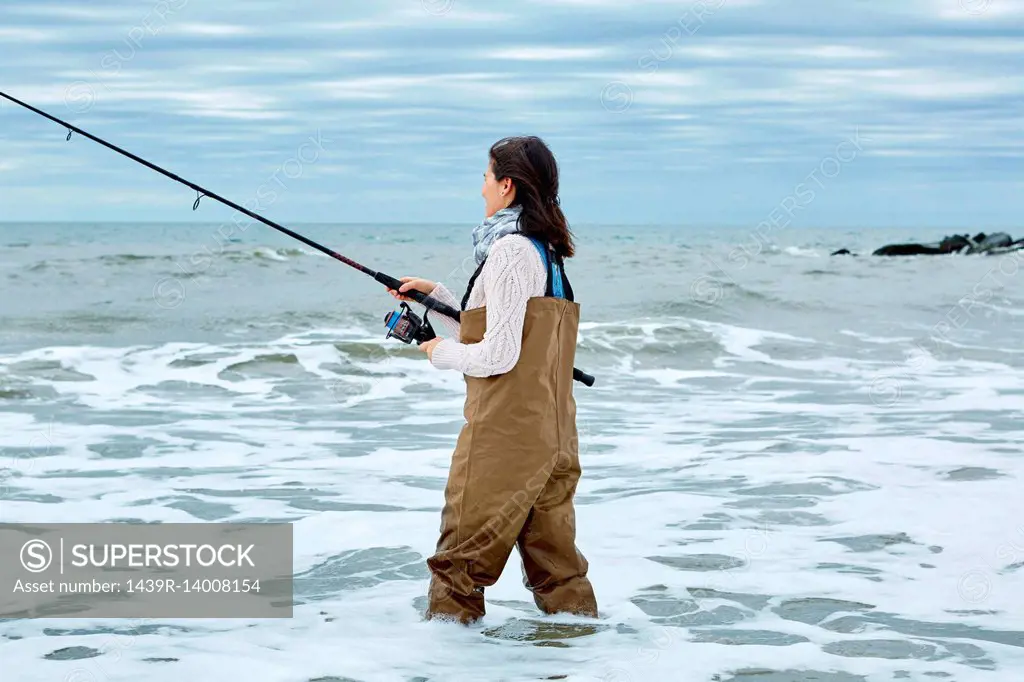 Young woman in waders sea fishing knee deep in water - SuperStock