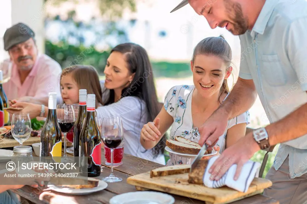 Man slicing bread at outdoor family lunch
