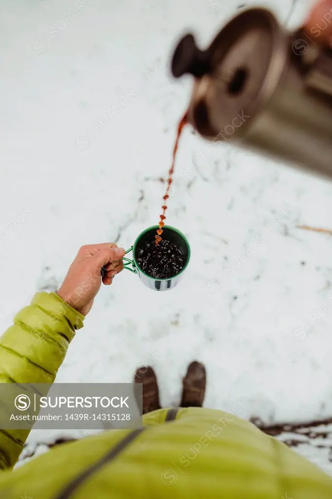 Personal perspective view of male hiker pouring coffee from flask in snow