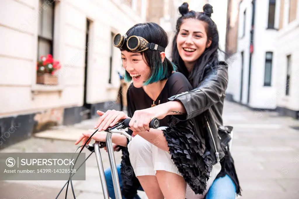 Two young stylish women cycling retro bicycle along street