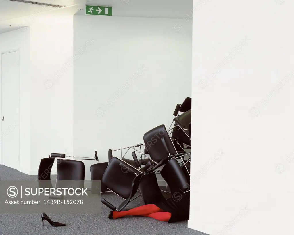 Businesswoman trapped beneath stack of chairs