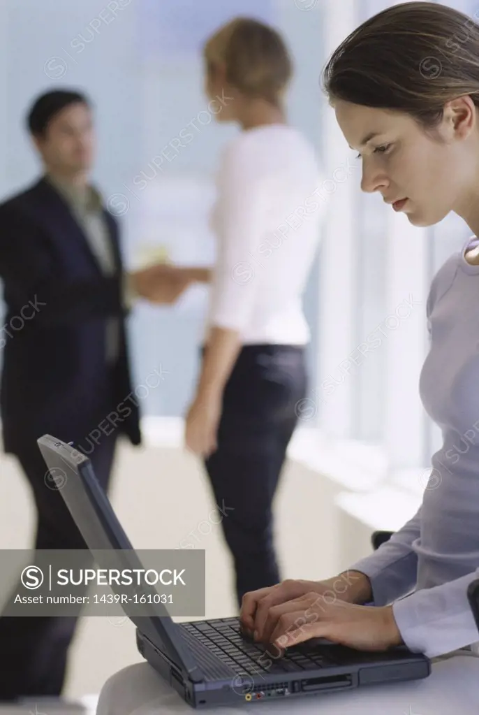 Woman using laptop as colleagues shake hands