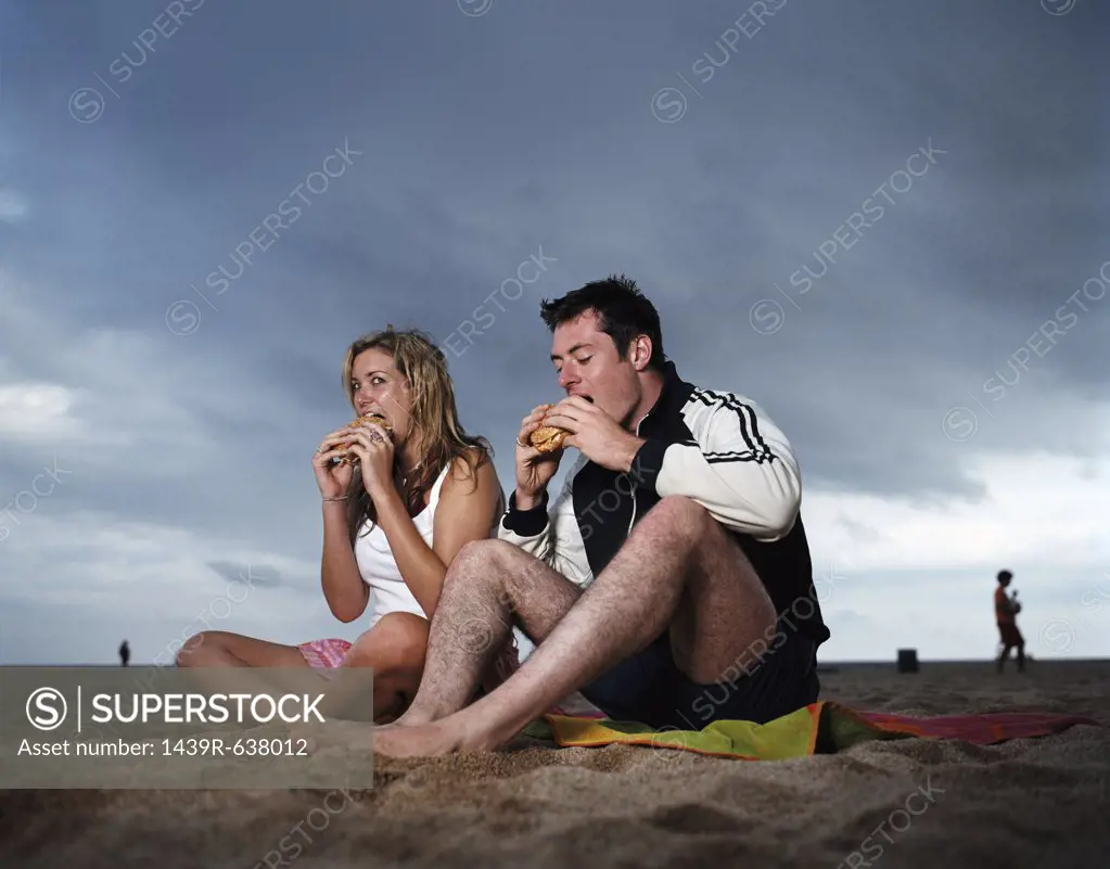 Couple eating hamburgers on beach