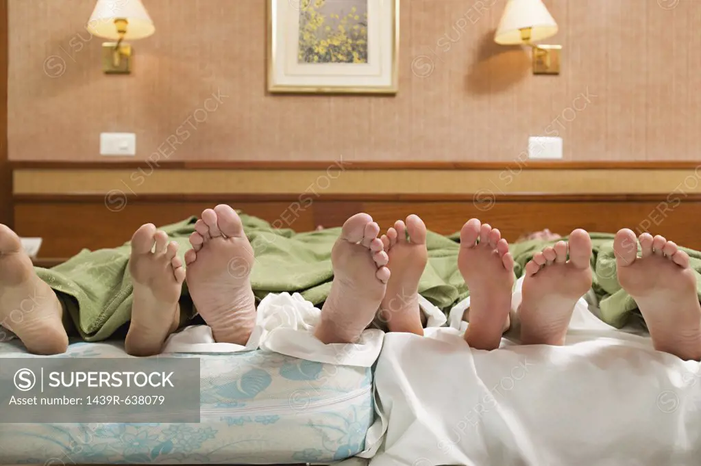 Four pairs of feet in a bed