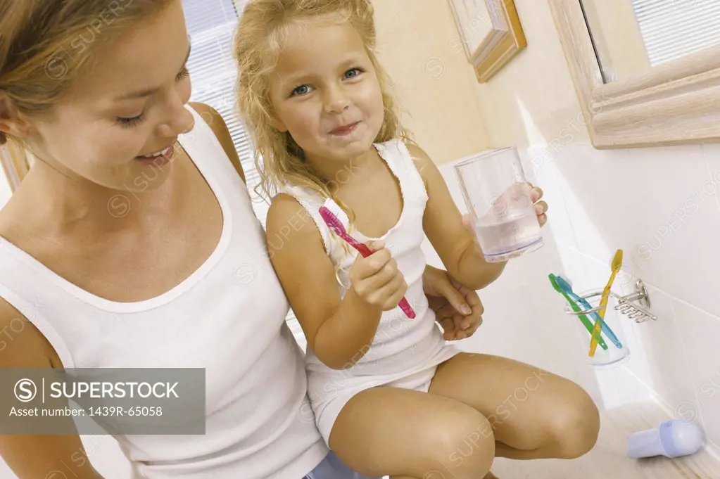 Mother helping daughter brush teeth