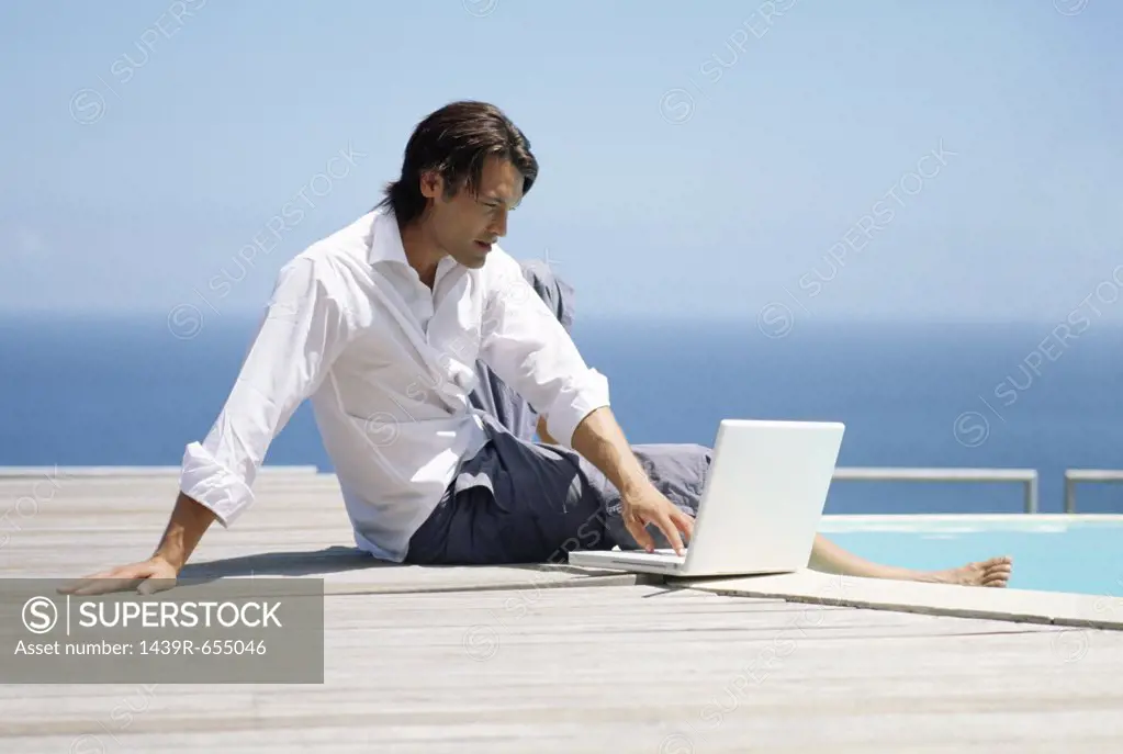 Man with laptop by swimming pool