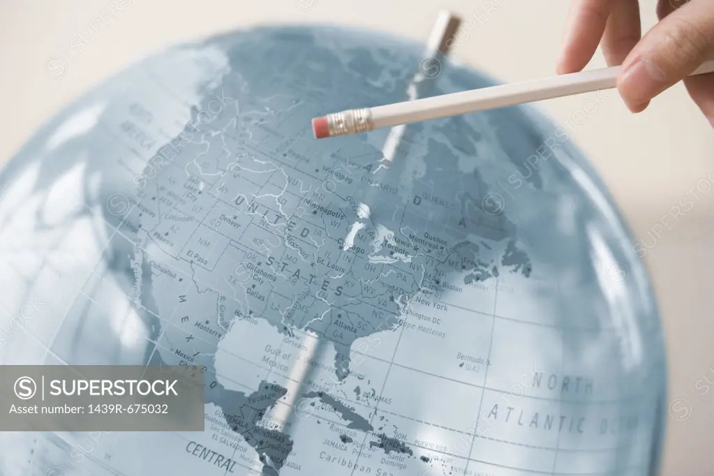 Person pointing at a globe with a pencil
