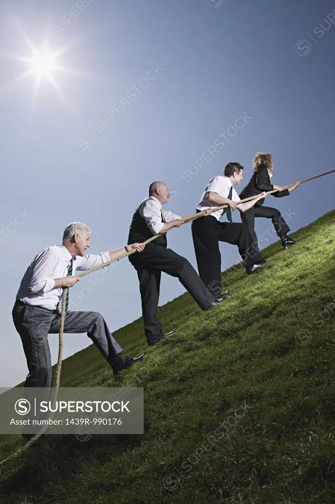 Business people climbing hill with rope
