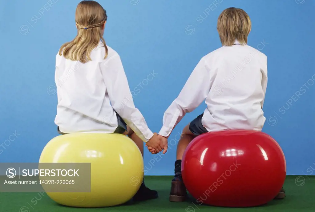 Girl and boy sitting on exercise balls holding hands