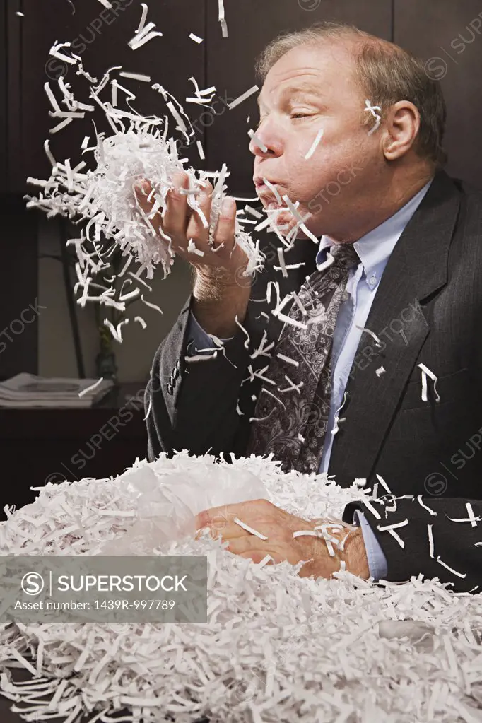 Mature businessman playing with paper shreddings