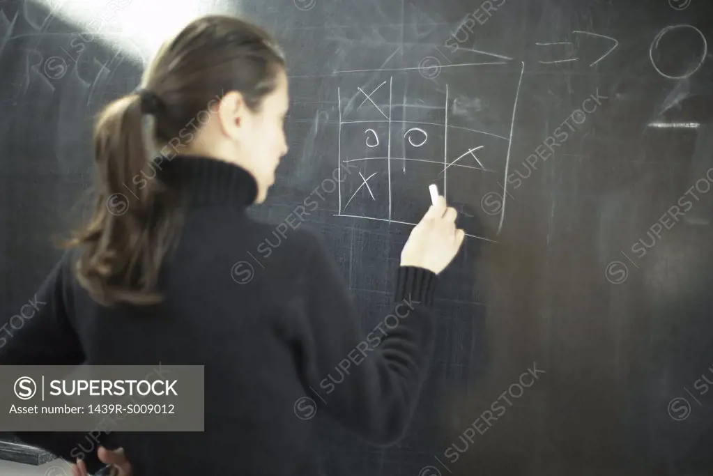 Young woman drawing noughts and crosses on a blackboard