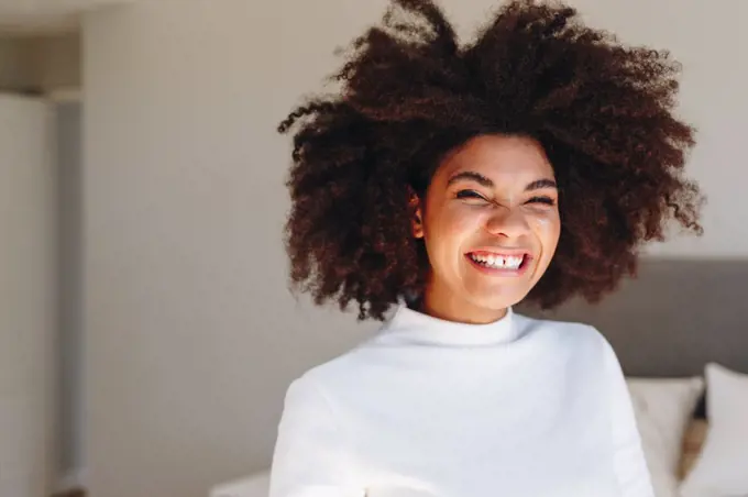 Young woman with afro hairstyle laughing in bedroom, head and shoulder portrait
