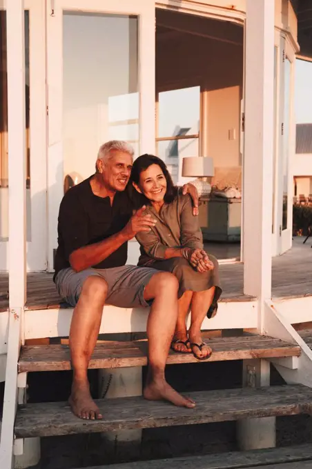 Senior couple enjoying sunset on steps in front of beach house