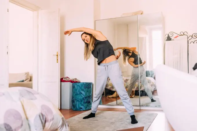 Italy, Young woman stretching at home