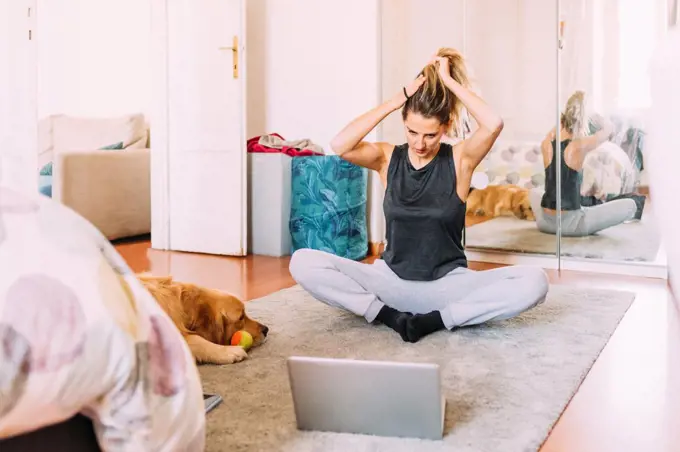 Italy, Young woman stretching in front of laptop on floor