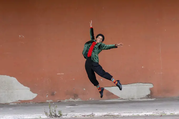 Italy, Tuscany, Pistoia, Smiling woman jumping against wall