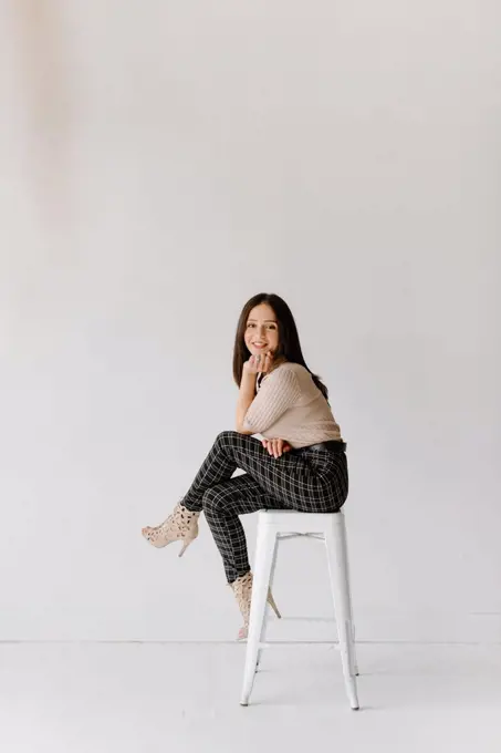 Studio shot of young woman sitting on stool