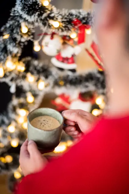 Close-up of person holding mug with coffee in front of Christmas tree