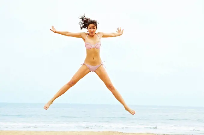 Young woman in bikini doing star jump on beach