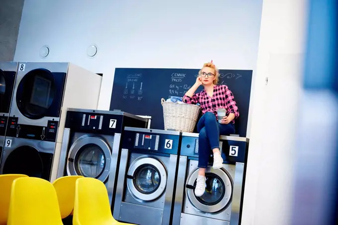 Bored woman sitting on top of washing machine at laundrette