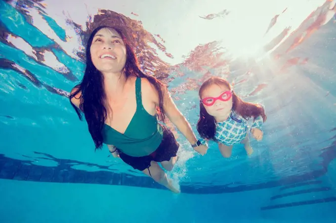Underwater view of mature woman swimming holding daughter's hand