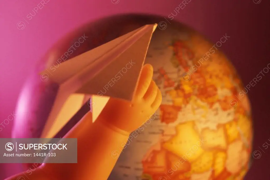 Close-up of a doll's hand holding a paper plane near a globe