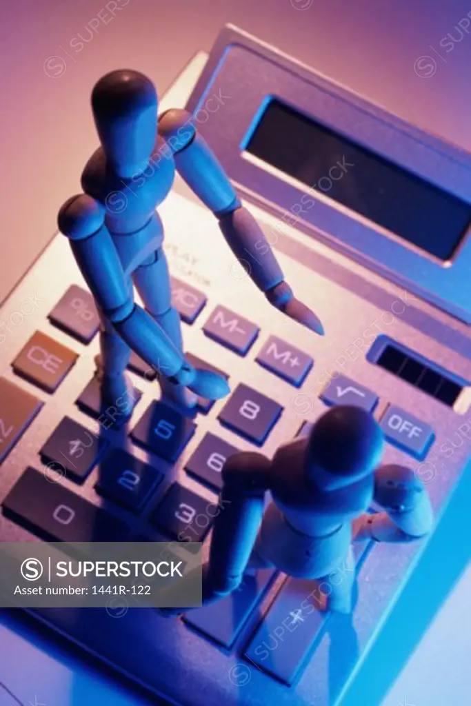 Close-up of two wooden dolls on a calculator