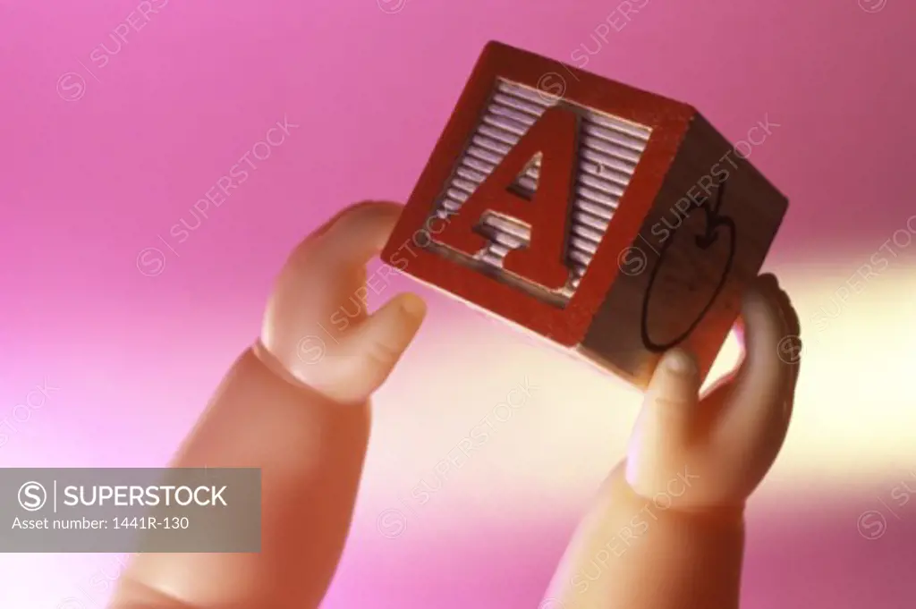 Close-up of a doll's hands holding a wooden block
