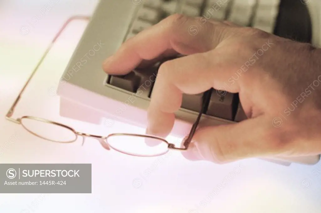 Close-up of a person holding eyeglasses on a computer keyboard