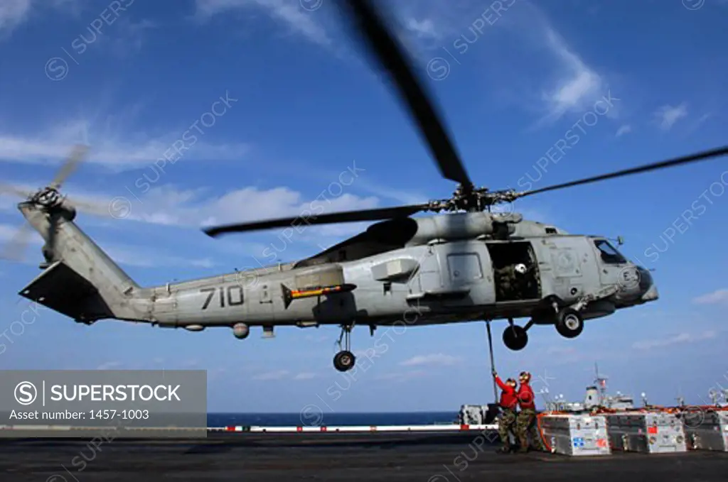 Two aviation ordnance men connecting a transport cable to a military helicopter on the deck of a aircraft carrier, USS Kitty Hawk, December 6, 2006