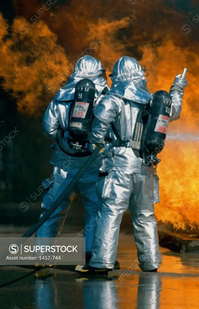 Rear view of two firefighters extinguishing a fire