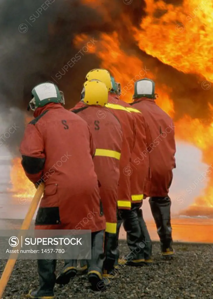 Rear view of five firefighters extinguishing fire