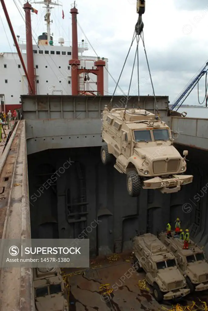 A harbor crane lifts a mine-resistant, ambush-protected vehicle from the hull of a cargo vessel.