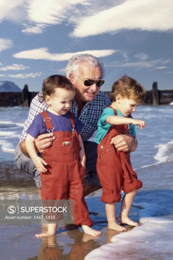 Grandfather holding his grandsons at the beach