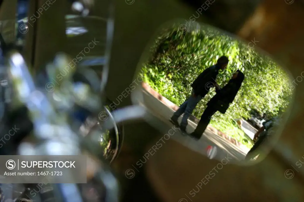 Reflection of a young couple in the side view mirror of a motorcycle