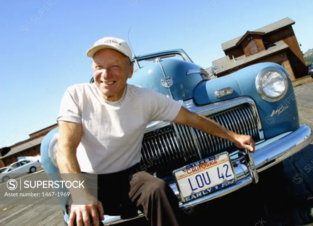 Close-up of a senior man sitting on the bumper of a vintage car