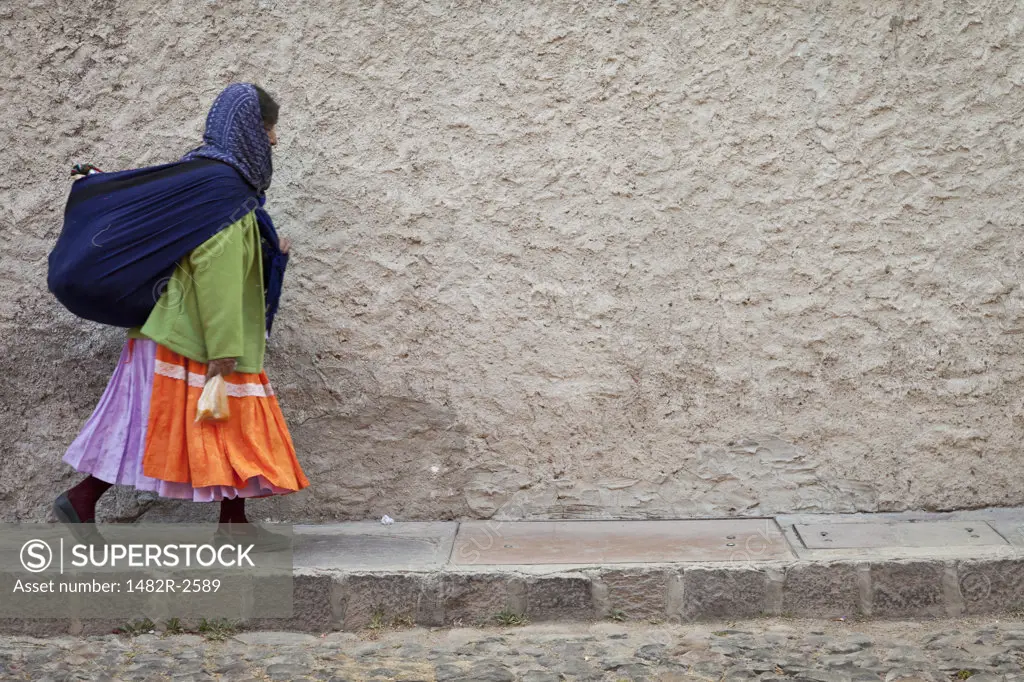 Mexico, Guanajuato, San Miguel de Allende, Woman wearing traditional clothing walking down narrow sidewalk