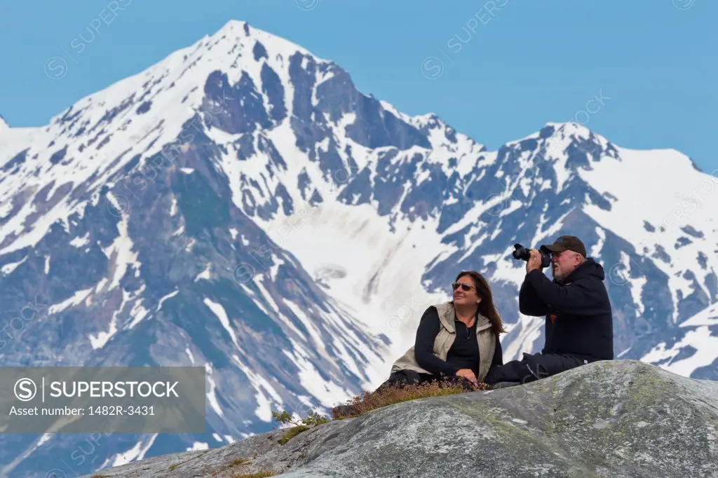 Couple sitting on a rock and photographing, Reid Glacier, Glacier Bay National Park, Alaska, USA