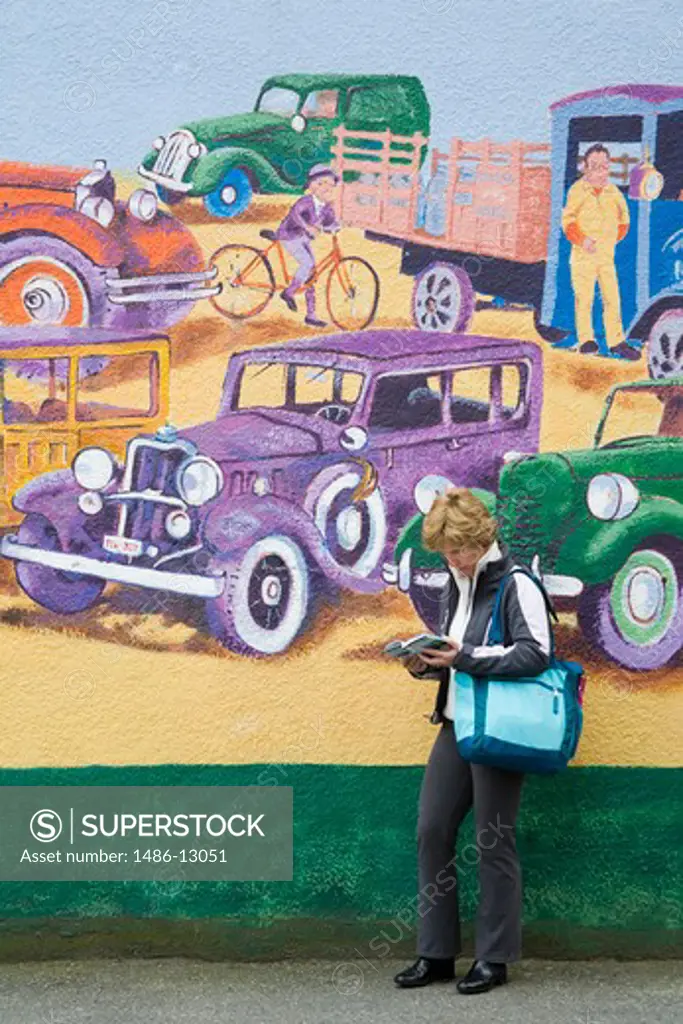 Canada, British Columbia, Vancouver, Commercial Drive, woman standing by mural by Elizabeth Hollick