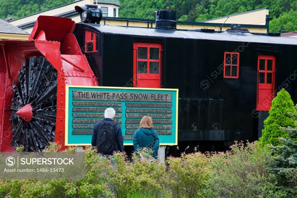 Tourists reading a signboard in front of a snowplow, White Pass and Yukon Route, Skagway, Alaska, USA