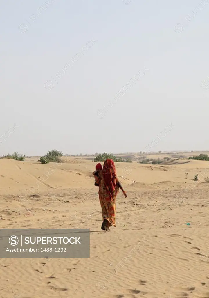 India, Rajahstan, Jaisalmer, Thar Desert, Sam Dunes, Woman with baby walking in desert